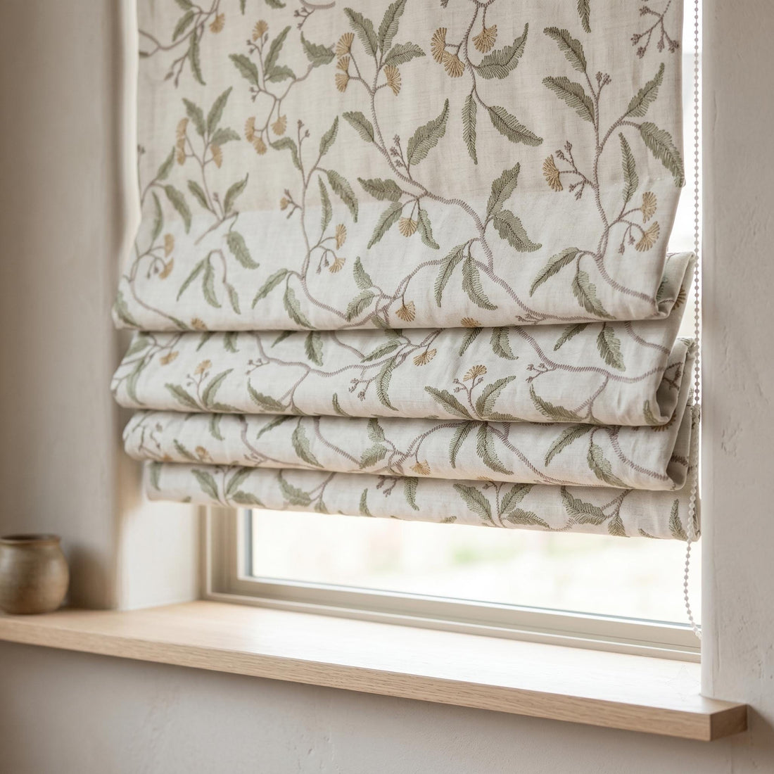 Close-up of ivory linen Roman shade folds with sage green leaves, taupe vines, and beige floral embroidery.